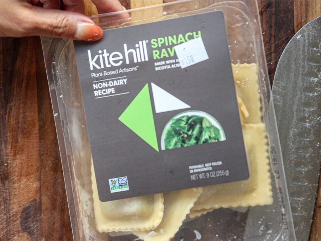 Creamy Cozy Kale White Bean Soup (EASY & Vegan). 13 A hand holds a package of Kite Hill Spinach Ravioli, labeled as a non-dairy, plant-based, and non-GMO product. Some ravioli pieces are visible inside the clear plastic container.