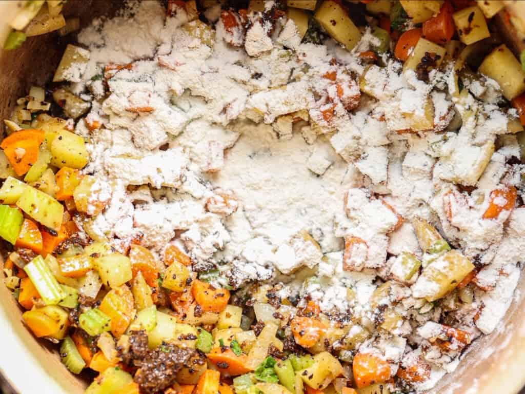 Creamy Cozy Kale White Bean Soup (EASY & Vegan). 19 Diced carrots, celery, and potatoes are sautéed in a pot with visible specks of flour sprinkled on top, preparing the base for a savory dish.