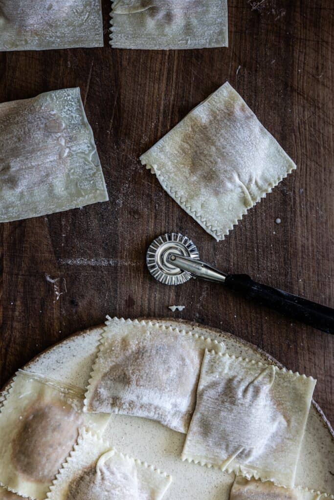 The Korean Vegan: HomeMade 17 Homemade ravioli squares cut with a decorative cutter rest on a wooden surface. Some are plated, while others await preparation in this rustic kitchen. The Korean vegan twist adds an exciting cultural flair to these traditional pasta delights.