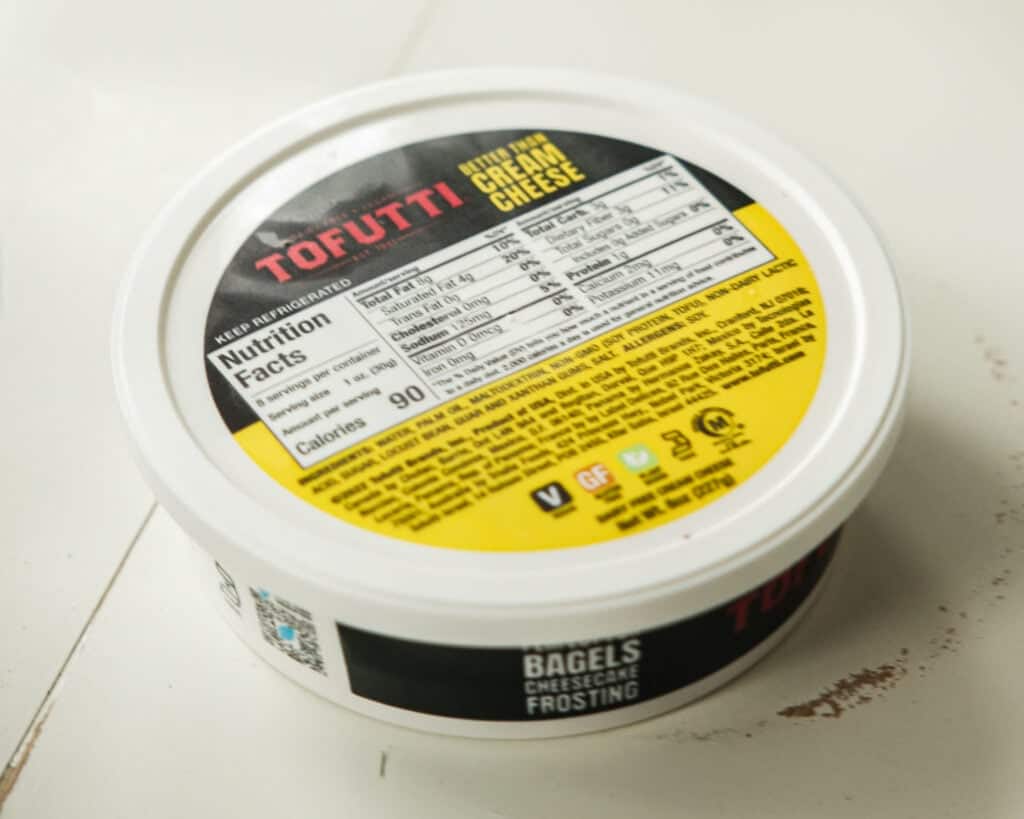 Pink Strawberry Crème Brûlée (Vegan & Easy) 3 A round container of Tofutti Better Than Cream Cheese sits on a white surface, its yellow and black lid displaying nutrition facts and ingredients—perfect for creating easy crème brûlée or vegan crème brûlée treats at home.