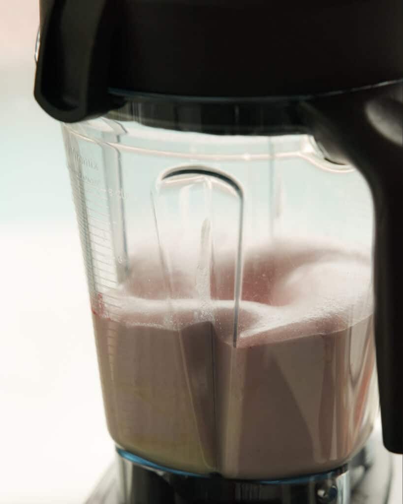 Pink Strawberry Crème Brûlée (Vegan & Easy) 10 A close-up of a blender mixing a light purple smoothie, with froth forming on the surface and visible measurement markings on the blender jar—perfect for an easy recipe or as inspiration for your next vegan dessert.