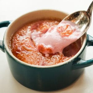 Pink Strawberry Crème Brûlée (Vegan & Easy) 16 A spoon scoops pink, creamy Strawberry Crème Brûlée from a small, round blue dish filled with a caramelized, glazed topping.