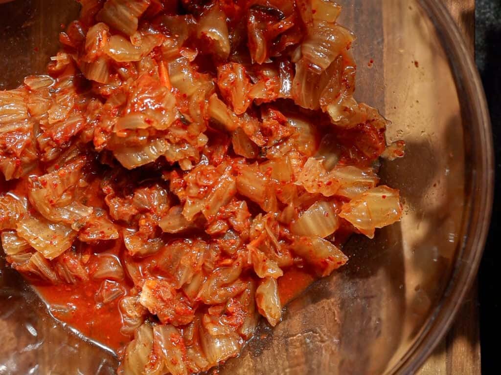 Easy and Crispy Korean Kimchi Pancakes (김치전) Recipe. 7 Chopped kimchi in a glass bowl, featuring spicy red chili paste coating pieces of fermented cabbage.
