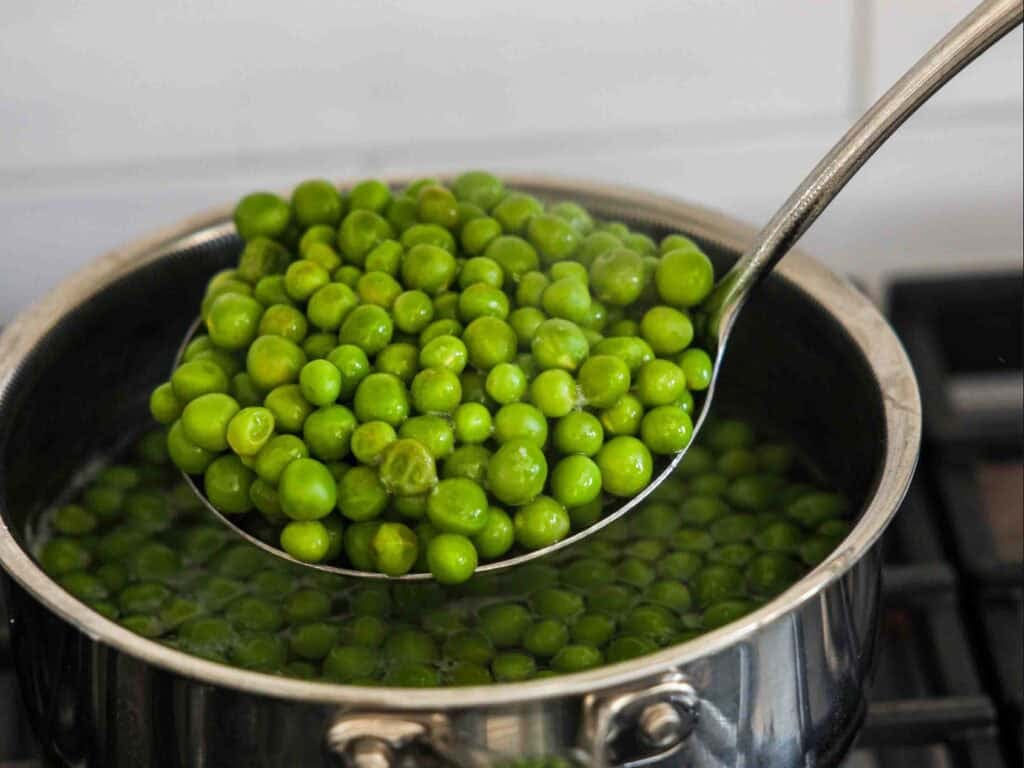 The BEST Sweet Green Pea Risotto Recipe (Vegan). 9 A metal ladle lifts bright green peas out of a pot of boiling water on a stove, with steam rising from the pot.