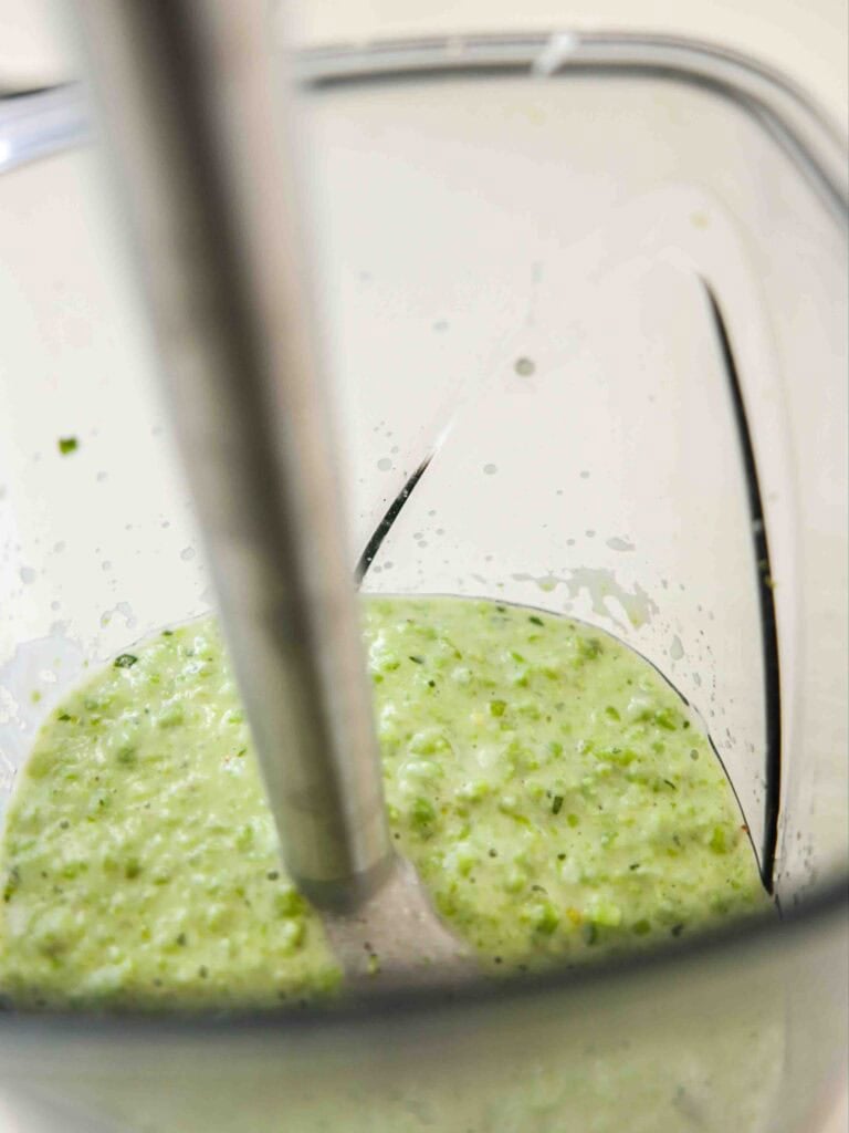 The BEST Sweet Green Pea Risotto Recipe (Vegan). 11 Close-up of a hand blender blending a creamy, green mixture with small chunks inside a transparent blender container.