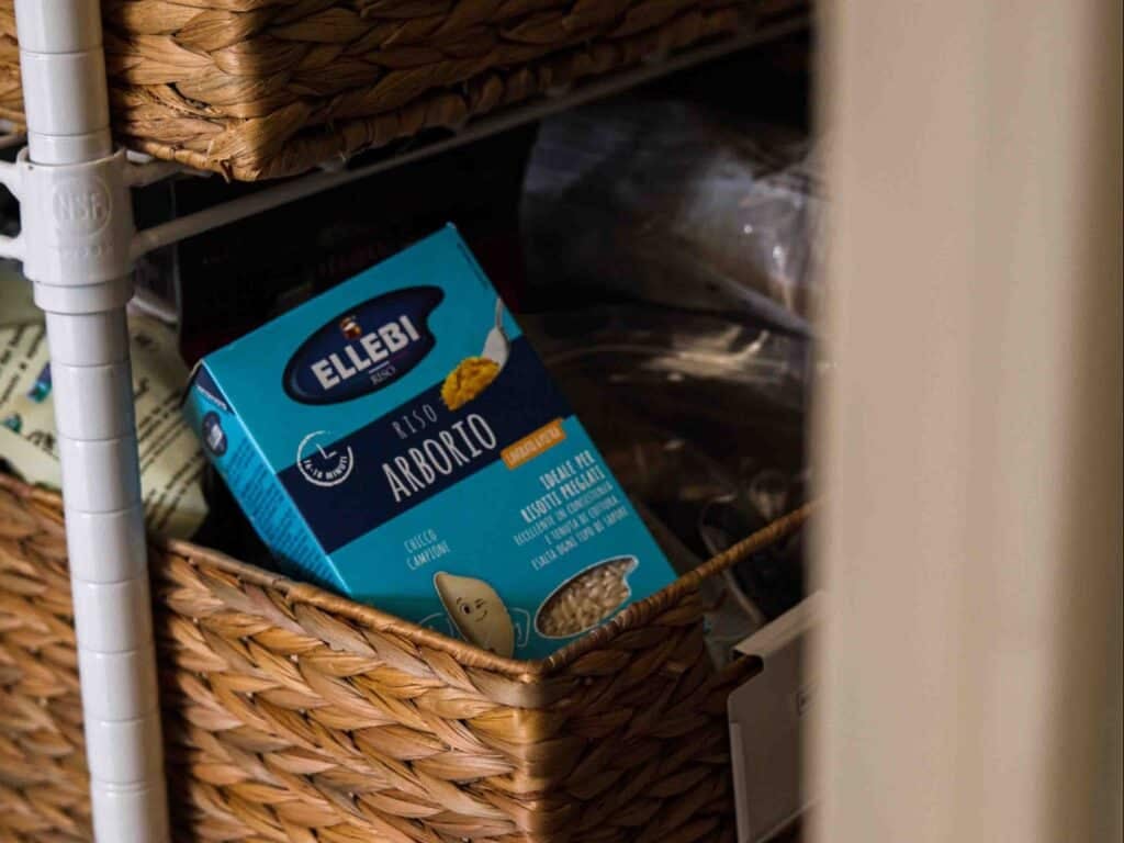 The BEST Sweet Green Pea Risotto Recipe (Vegan). 4 A blue box of Ellebi Arborio rice is stored in a woven basket on a pantry shelf, surrounded by other food items.