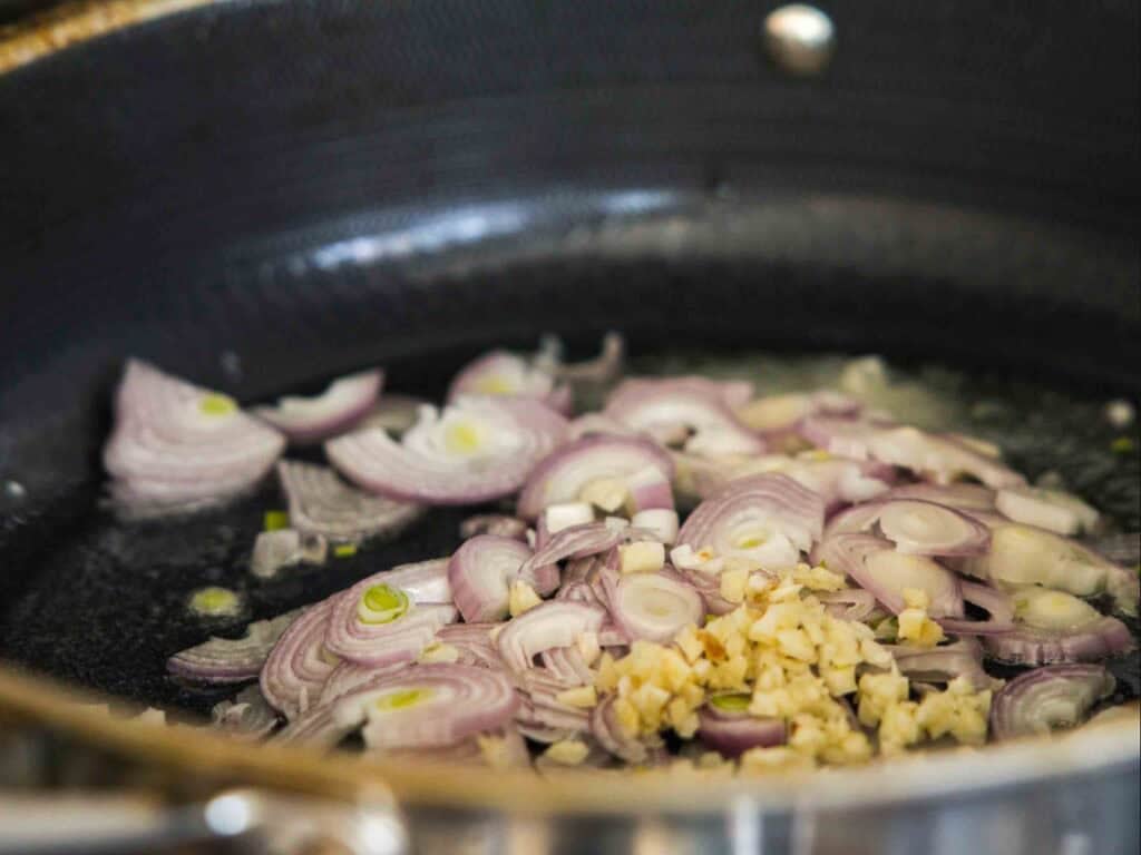 The BEST Sweet Green Pea Risotto Recipe (Vegan). 12 Sliced shallots and minced garlic are being sautéed in a pan with oil as the aromatic base for a flavorful green pea risotto.