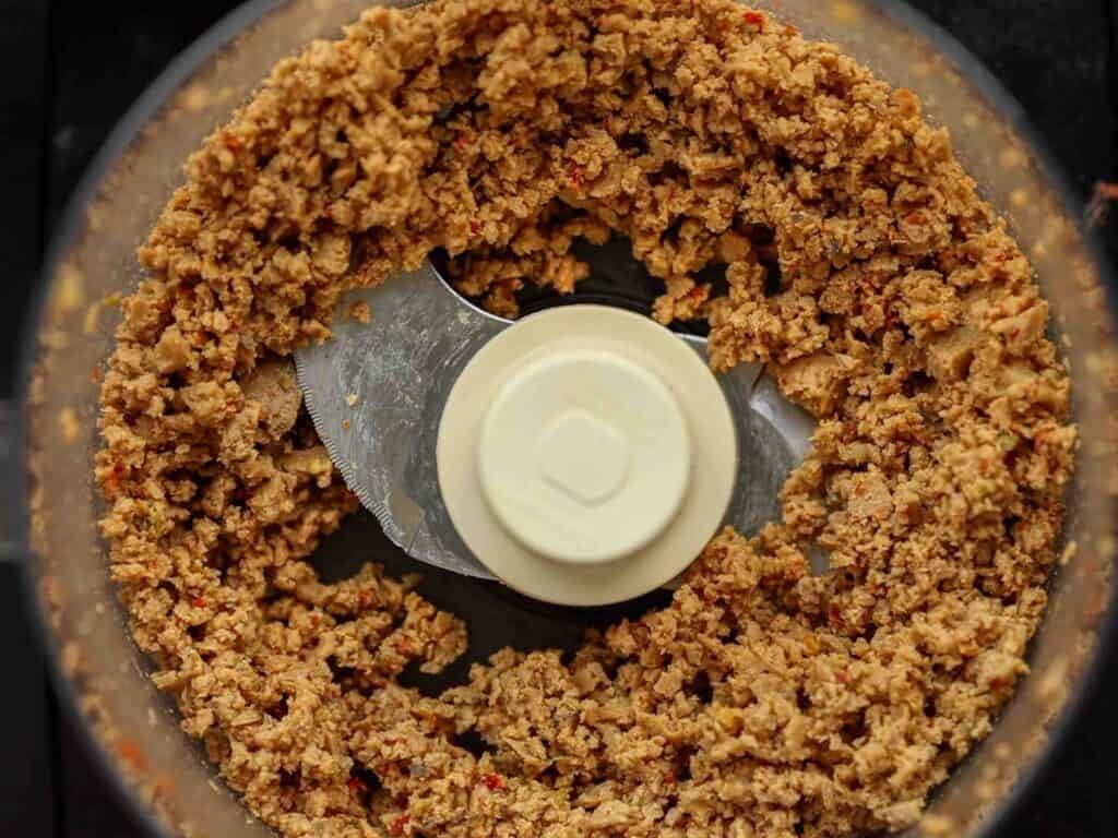 BEST Vegan Bolognese Recipe - Meaty and Delicious. 25 Close-up of a food processor containing finely chopped, vegan sausage, with metal blades in the center and food evenly distributed around the edges.