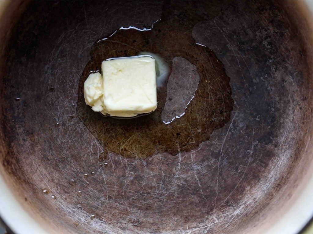 BEST Vegan Bolognese Recipe - Meaty and Delicious. 26 A cube of vegan butter melting in a large, well-used pan, with liquid butter starting to spread around it.
