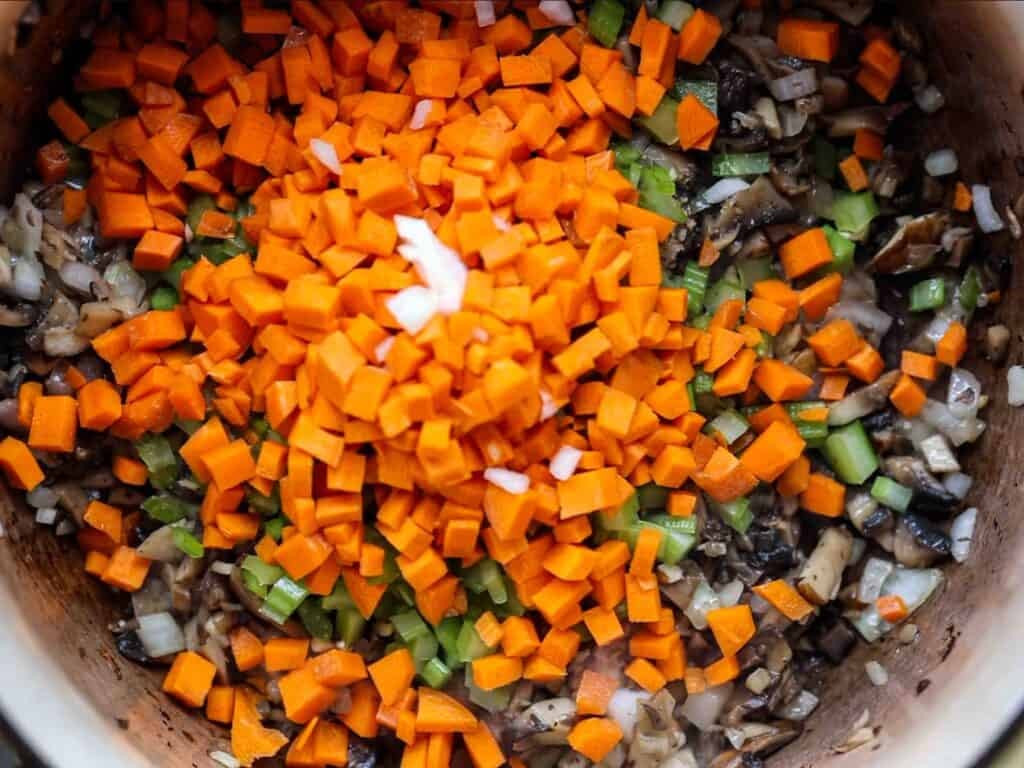 BEST Vegan Bolognese Recipe - Meaty and Delicious. 28 Diced carrots, celery, onions, and mushrooms are piled and mixed together in a pot, showing the vibrant orange, green, white, and brown colors of the vegetables.
