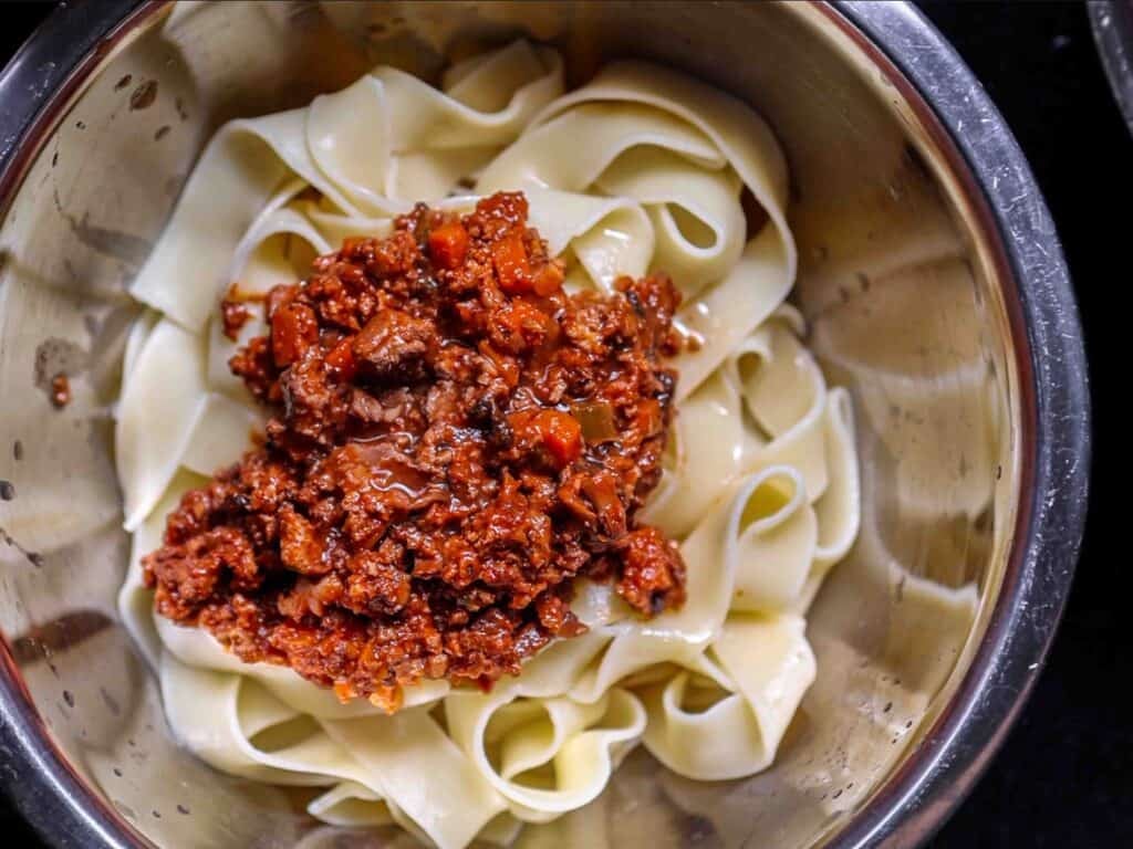 BEST Vegan Bolognese Recipe - Meaty and Delicious. 38 A bowl of wide, flat pasta noodles topped with a generous portion of hearty vegan bolognese sauce, featuring visible pieces of plant-based ground and diced vegetables.