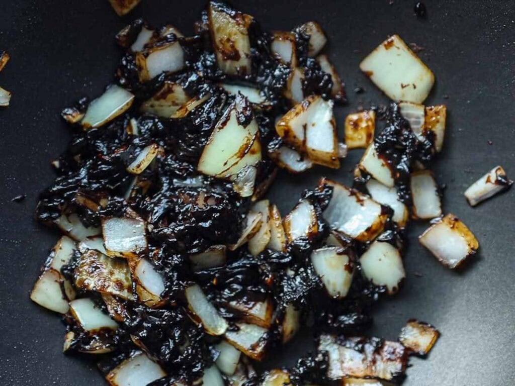 Diced onions sautéed in a pan, some pieces caramelized and browned, creating a mix of golden and dark brown colors.