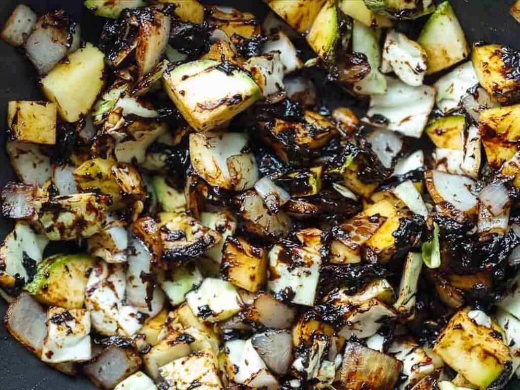 DELICIOUS Jjajangmyeon Recipe-Korean Black Bean Noodles. 38 Chopped zucchini and onions being sautéed in a pan, with the vegetables caramelized and browned, showing a mix of green, white, and dark brown colors.
