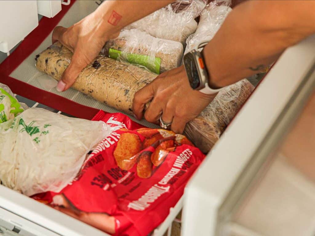BEST Bakery Style Vegan Chocolate Chip Cookies Recipe. 13 A person’s hands arranging wrapped food and frozen packages inside a freezer drawer, with some items covered in plastic and some in red packaging.