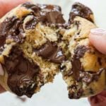30+ AMAZING VEGAN Holiday Recipes Everyone's gonna Love. 29 Close-up of hands pulling apart a warm, gooey vegan chocolate chip cookie, with melted chocolate oozing from the center.