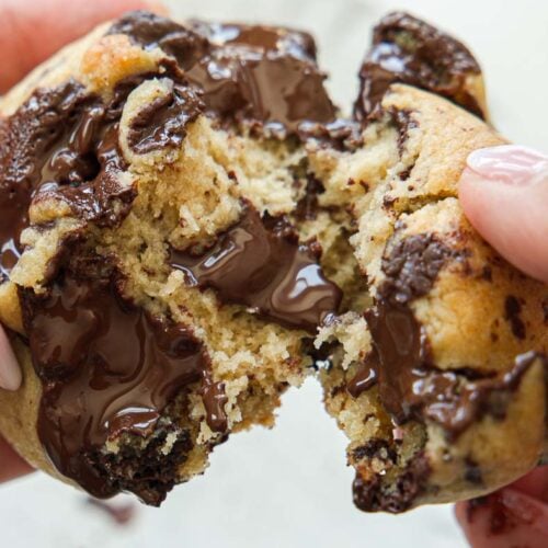 BEST Bakery Style Vegan Chocolate Chip Cookies Recipe. 19 Close-up of hands pulling apart a warm, gooey vegan chocolate chip cookie, with melted chocolate oozing from the center.