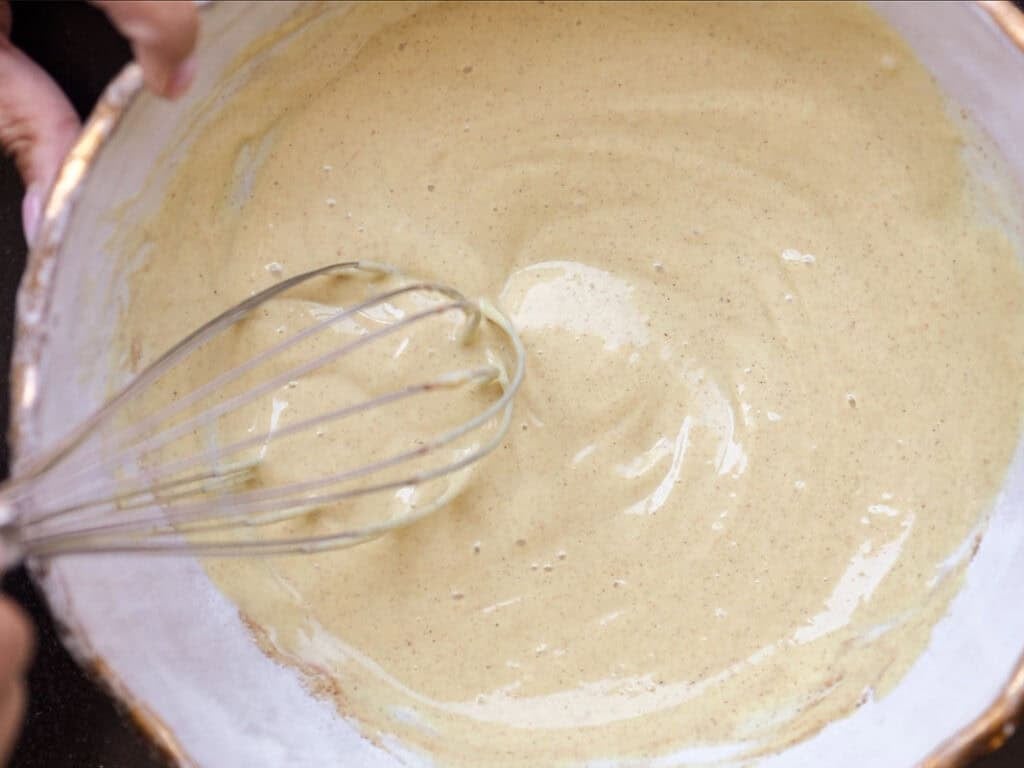 5-Ingredient Vegan French Toast Recipe - Fast & Easy! 5 A close-up of a person whisking smooth, light yellow batter in a white bowl.