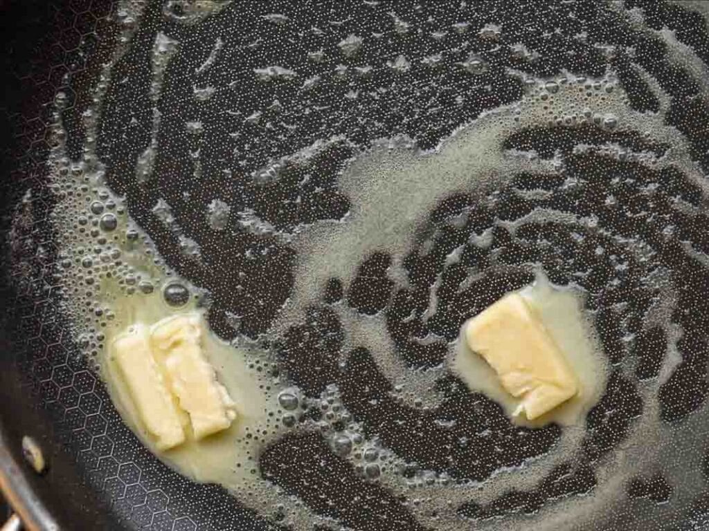 5-Ingredient Vegan French Toast Recipe - Fast & Easy! 8 Two pieces of butter melting in a frying pan, creating swirls of melted butter and bubbles on the pans surface.