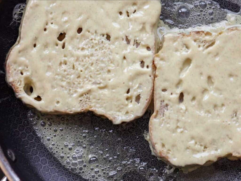 5-Ingredient Vegan French Toast Recipe - Fast & Easy! 9 Two slices of bread coated in a batter are being cooked in a frying pan with melted butter, likely in the process of making French toast.