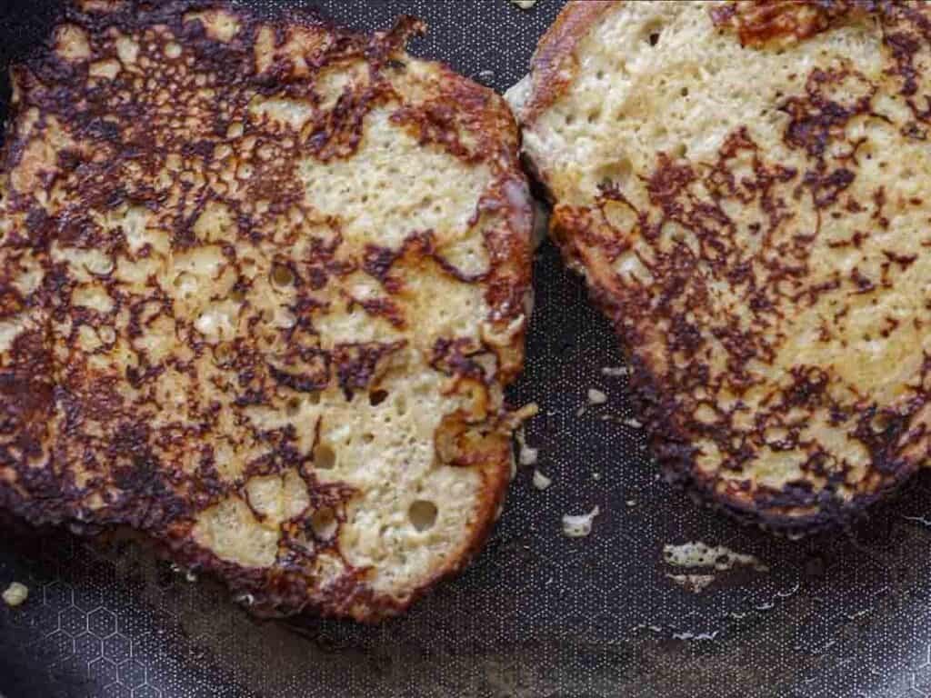 5-Ingredient Vegan French Toast Recipe - Fast & Easy! 10 Two slices of vegan French toast are cooking in a skillet, with golden brown, slightly crispy surfaces and some visible bubbles and texture on the bread.