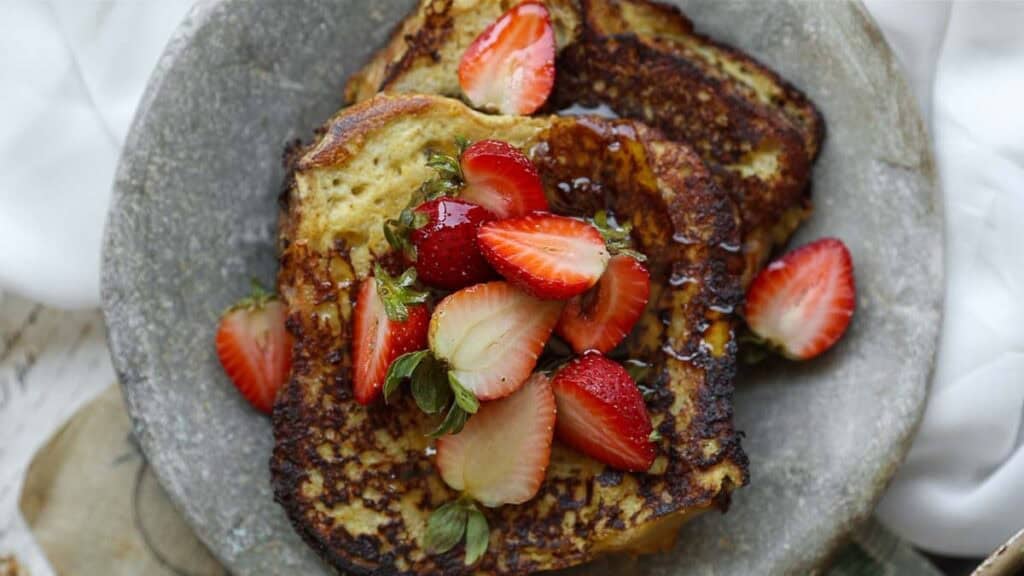 5-Ingredient Vegan French Toast Recipe - Fast & Easy! 1 Two slices of vegan French toast on a gray plate, topped with fresh sliced strawberries and drizzled with syrup.