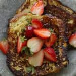 30+ AMAZING VEGAN Holiday Recipes Everyone's gonna Love. 56 Two slices of golden-brown vegan French toast topped with fresh strawberries and a drizzle of syrup, served on a gray plate.