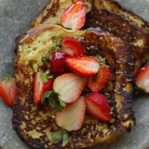 5-Ingredient Vegan French Toast Recipe - Fast & Easy! 12 Two slices of golden-brown vegan French toast topped with fresh strawberries and a drizzle of syrup, served on a gray plate.