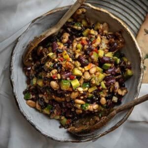 Viral Dense Bean Salad Recipe - Korean BBQ Style. 21 A bowl of colorful Korean BBQ dense bean salad with kidney beans, white beans, black beans, diced vegetables, and herbs, mixed and served with wooden salad utensils on a rustic plate.