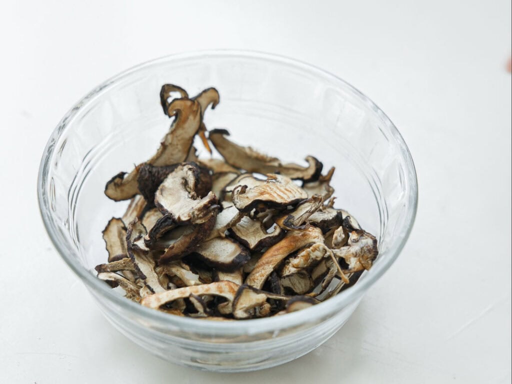 Viral Dense Bean Salad Recipe - Korean BBQ Style. 10 A clear glass bowl filled with dried mushroom slices sits on a white surface.