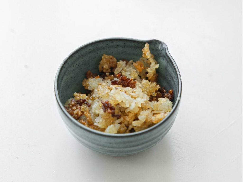 Viral Dense Bean Salad Recipe - Korean BBQ Style. 11 A small gray bowl filled with a mixture of cooked, crispy, golden-brown and white rice pieces, placed on a white surface.