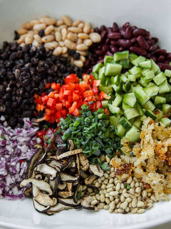 Viral Dense Bean Salad Recipe - Korean BBQ Style. 16 A bowl filled with chopped vegetables and beans, including cucumber, red bell pepper, red onion, black beans, kidney beans, white beans, pine nuts, green onions, sautéed mushrooms, and crispy cooked rice.