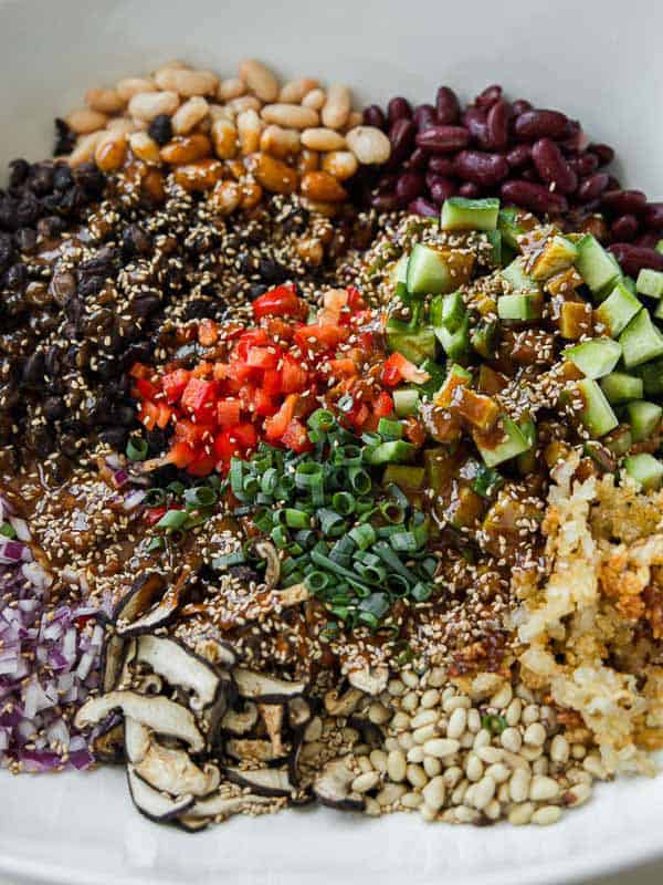 Viral Dense Bean Salad Recipe - Korean BBQ Style. 18 A colorful bowl with neatly arranged ingredients, including beans, diced cucumbers, red peppers, green onions, mushrooms, sesame seeds, pine nuts, chopped red onions, and crispy rice.