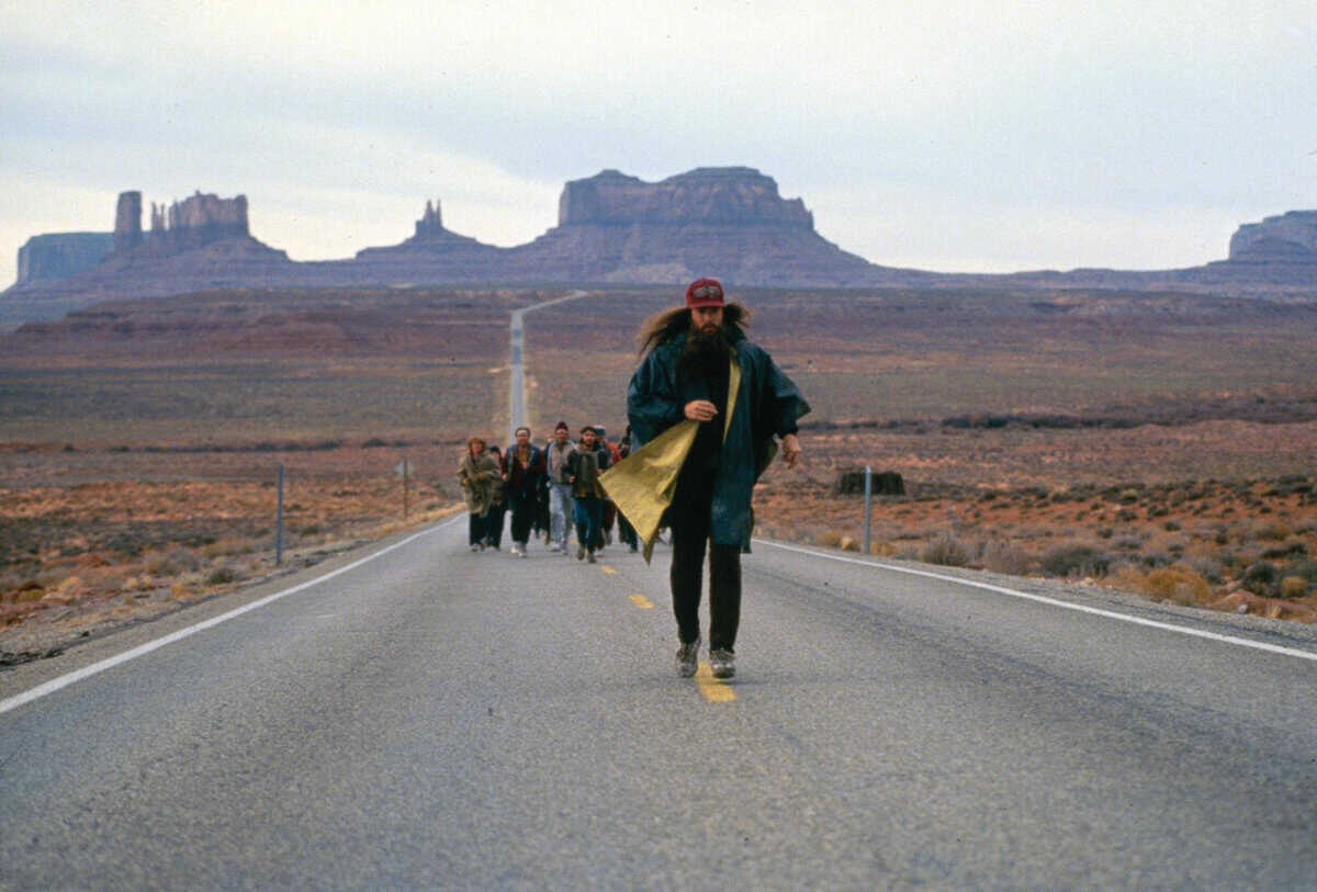 Can you be a runner if you hate running? 2 A man with long hair and a red cap runs down an empty desert highway, rock formations towering behind him, as a small group of runners follows his lead.