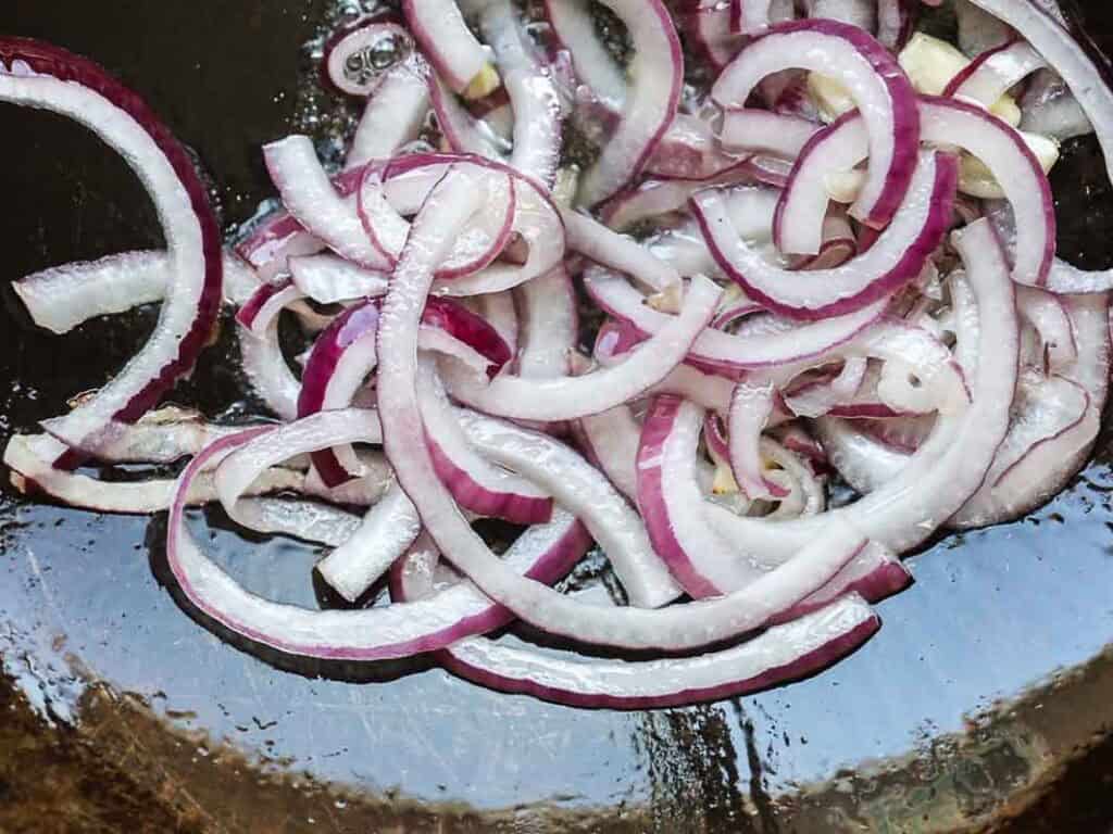 Easy & Healthy Lo Mein Vegan Recipe: Done in Minutes. 29 Sliced red onions cooking in a pan, starting to soften and turn translucent with some oil glistening around them.