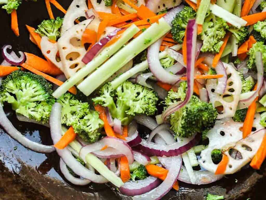 Easy & Healthy Lo Mein Vegan Recipe: Done in Minutes. 31 A colorful vegetable stir-fry with broccoli, red onion, carrot sticks, and sliced lotus root in a dark pan.