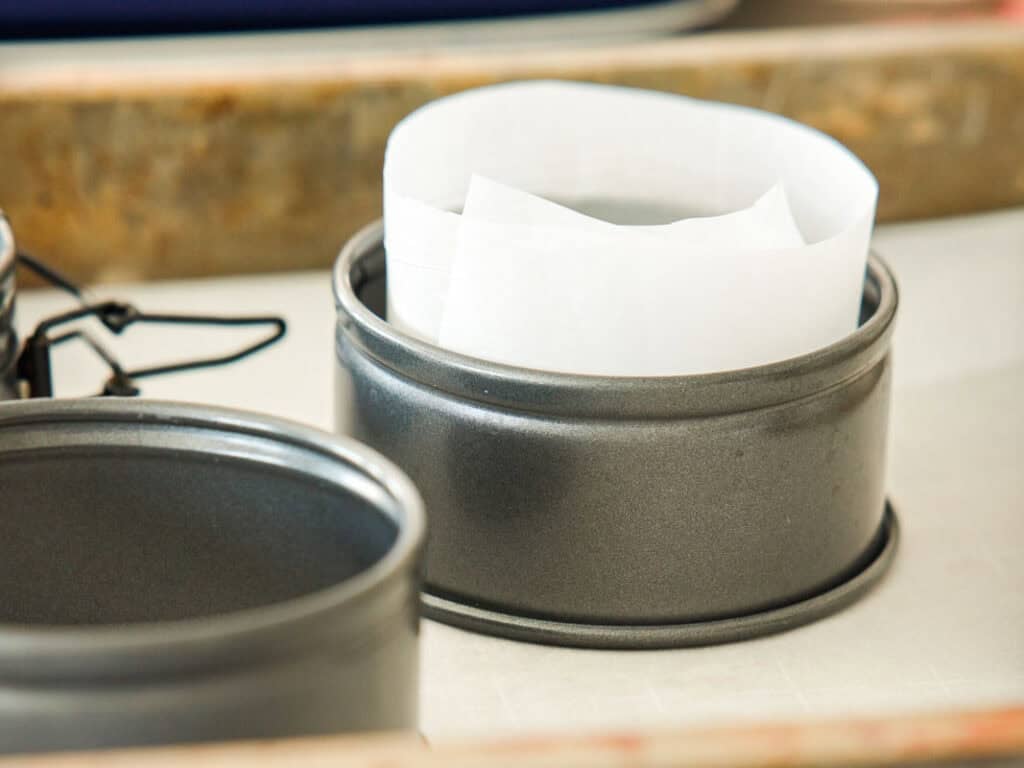 Easy & Delicious Vegan Chocolate Lava Cake Recipe. 31 A round metal baking pan with a strip of white parchment paper lining the inside, placed on a light surface with another similar pan nearby.