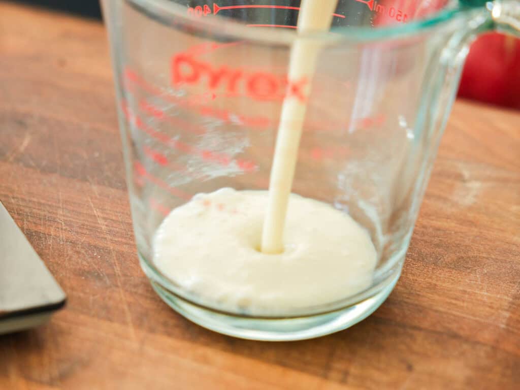 Easy & Delicious Vegan Chocolate Lava Cake Recipe. 35 Soy milk being poured into a clear glass Pyrex measuring cup, sitting on a wooden surface.