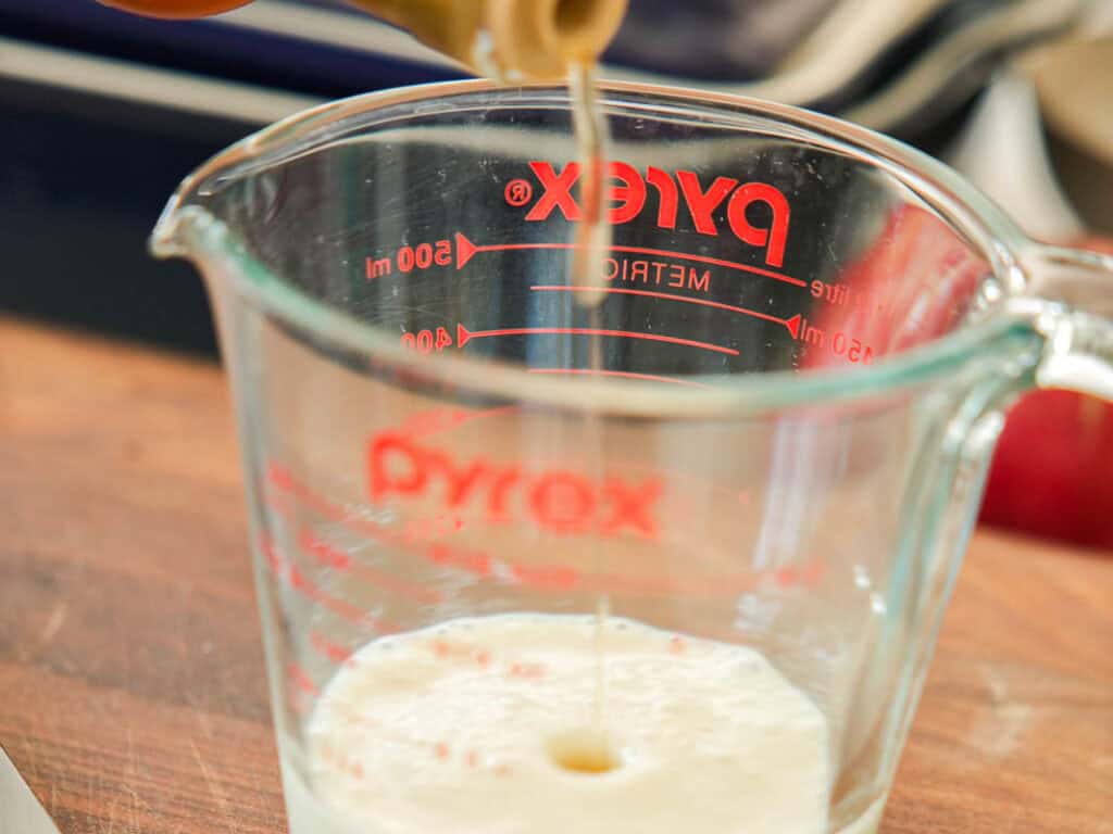 Easy & Delicious Vegan Chocolate Lava Cake Recipe. 36 A close-up of vinegar being poured into a Pyrex measuring cup on a wooden surface, with measurement markings visible on the glass.