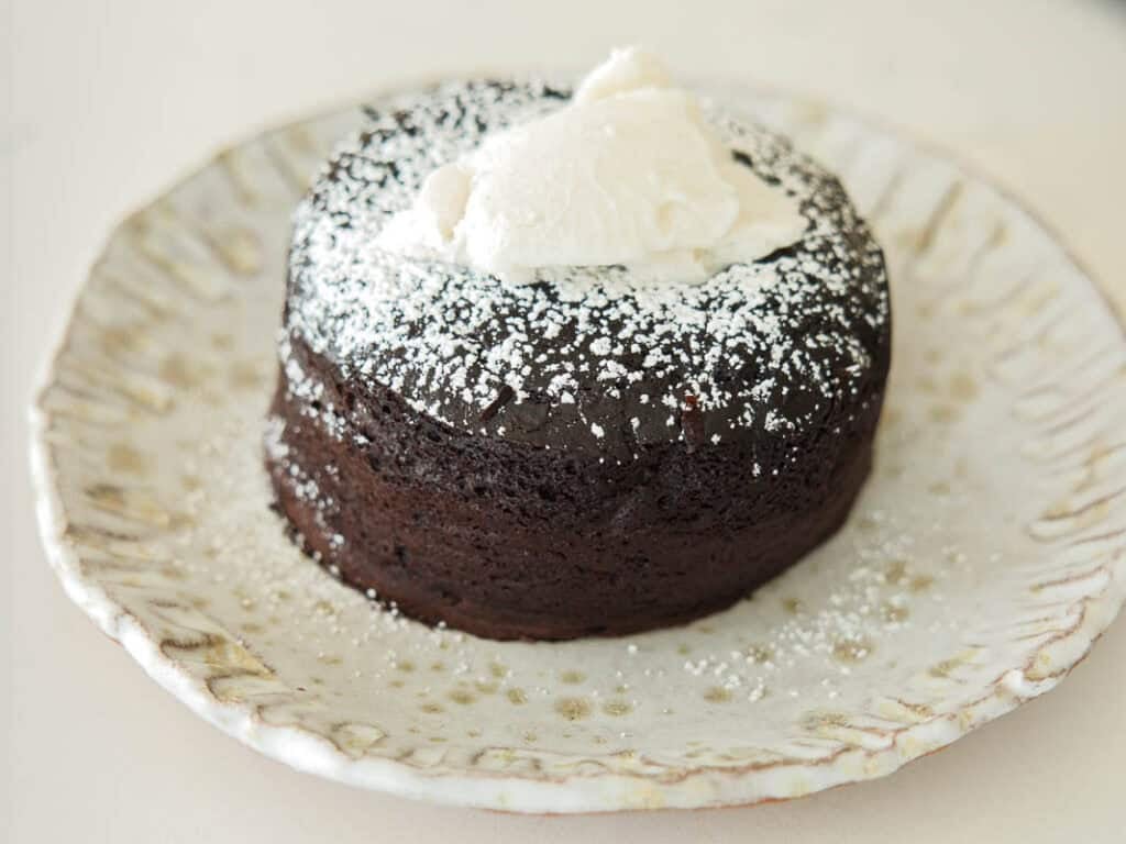 Easy & Delicious Vegan Chocolate Lava Cake Recipe. 18 A round vegan chocolate lava cake dusted with powdered sugar, topped with a dollop of whipped cream, served on a rustic, white ceramic plate.