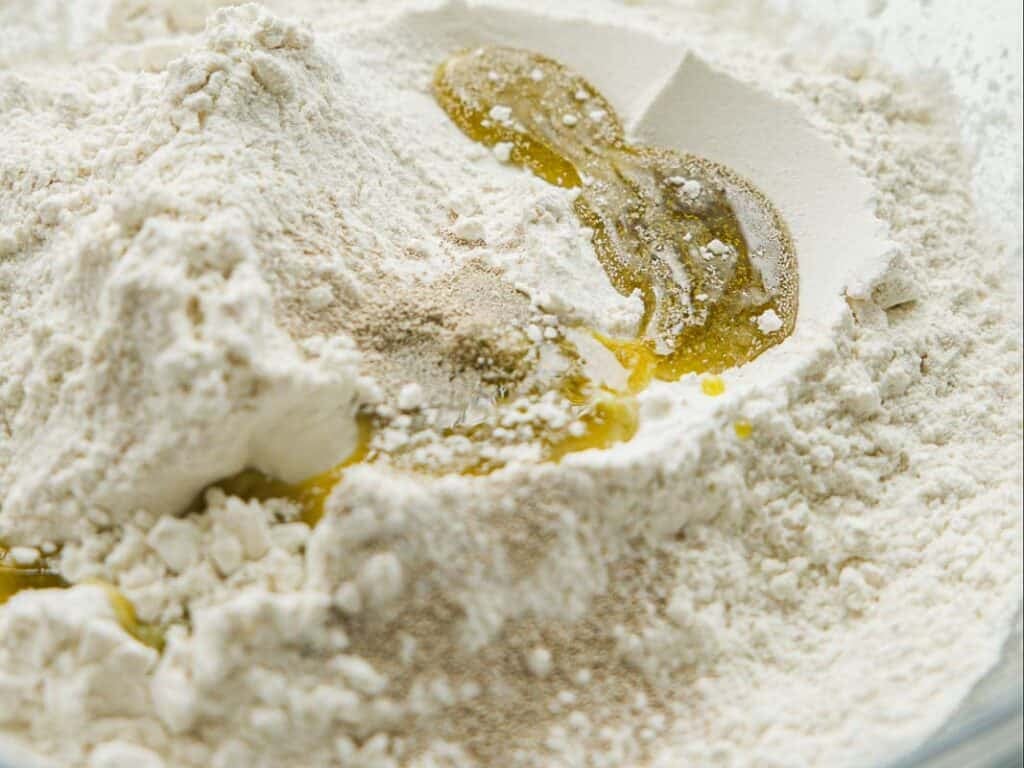 Close-up of flour, yeast, and olive oil in a mixing bowl, ready to be combined for baking.