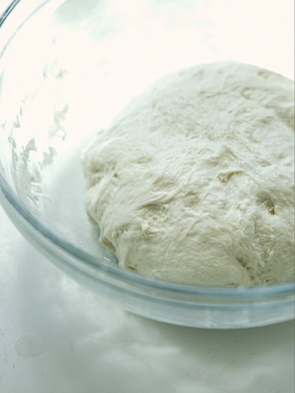 The Perfect Fluffy Focaccia Rossa Recipe - So Easy! 20 A close-up of a ball of risen dough in a clear glass bowl on a white surface, ready for baking.