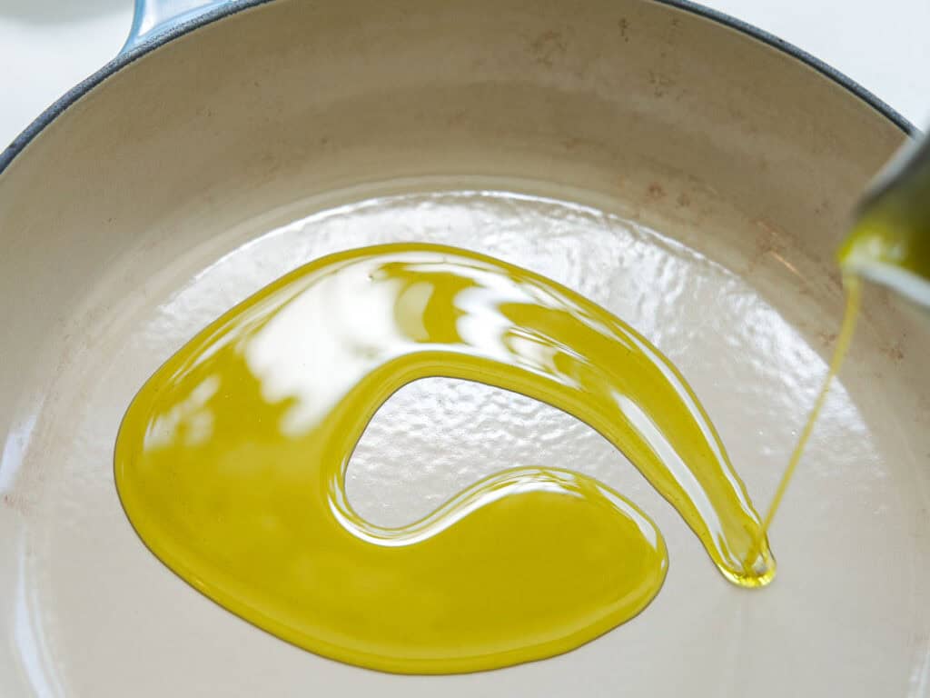 The Perfect Fluffy Focaccia Rossa Recipe - So Easy! 21 Olive oil being poured into a light-colored, empty skillet, forming a glossy swirl across the pan’s surface.