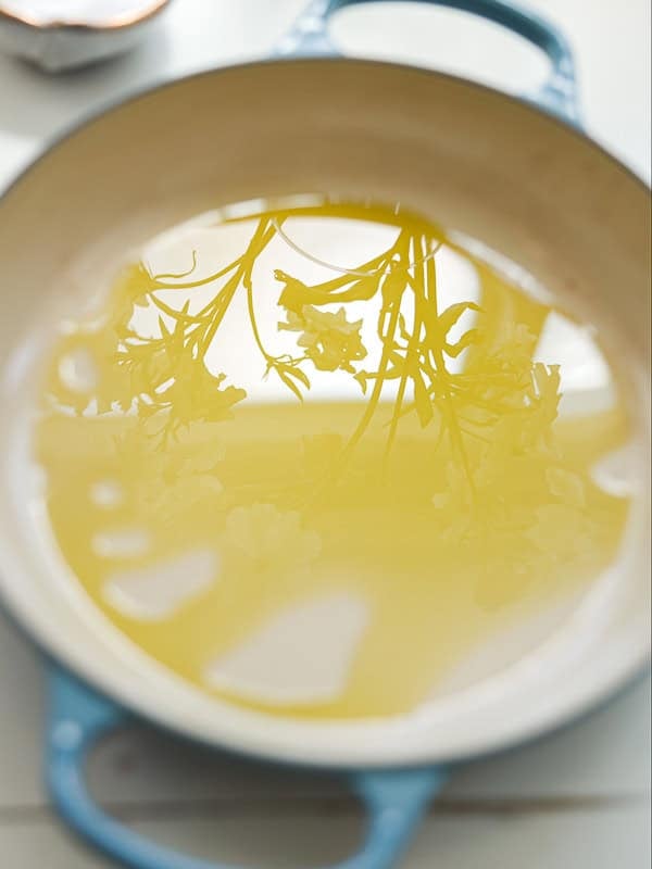 The Perfect Fluffy Focaccia Rossa Recipe - So Easy! 22 A close-up of a light blue pot filled with extra virgin olive oil, reflecting delicate white flowers and green stems on the surface of the liquid.