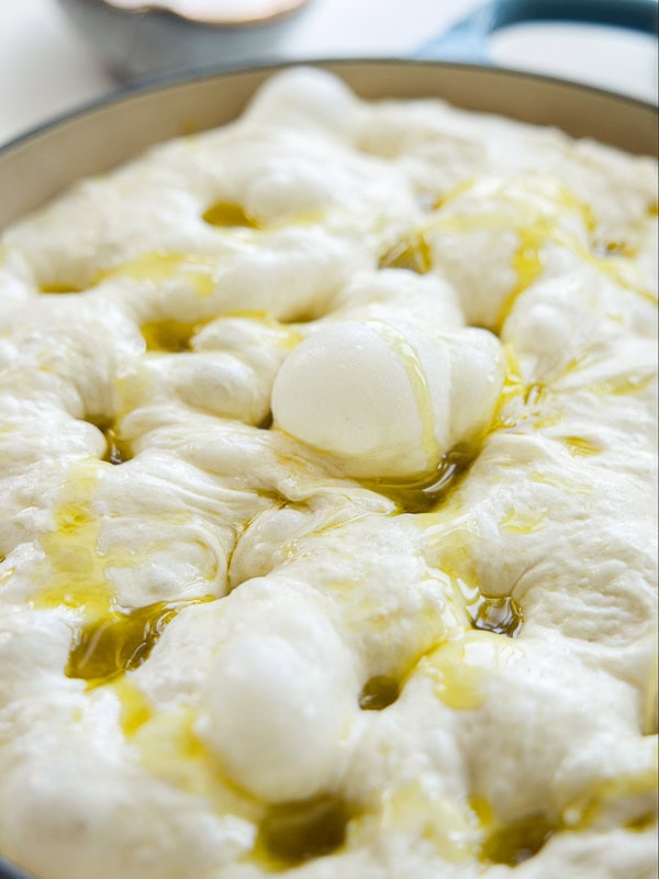 The Perfect Fluffy Focaccia Rossa Recipe - So Easy! 27 Close-up of soft, bubbly focaccia dough with dimples, drizzled with olive oil, in a round baking pan.