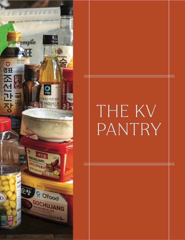 The Korean Vegan: HomeMade 54 A variety of Korean pantry staples, including sauces, canned corn, and condiments, arranged on a counter beside a red panel that reads THE KV PANTRY in white text—perfect for your next Book PreOrder cooking adventure.