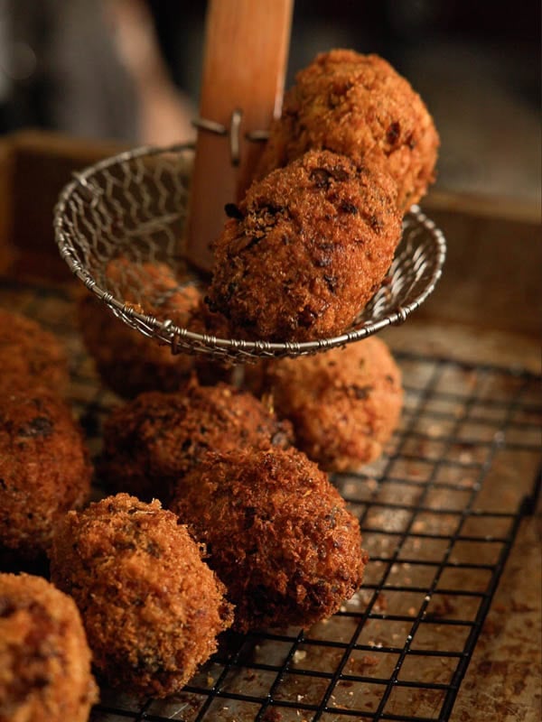 Delicious Supplì Inspired Kimchi Fried Rice Balls. 19 A wire skimmer lifts two golden-brown, crispy croquettes from a cooling rack holding several more croquettes on a baking tray.