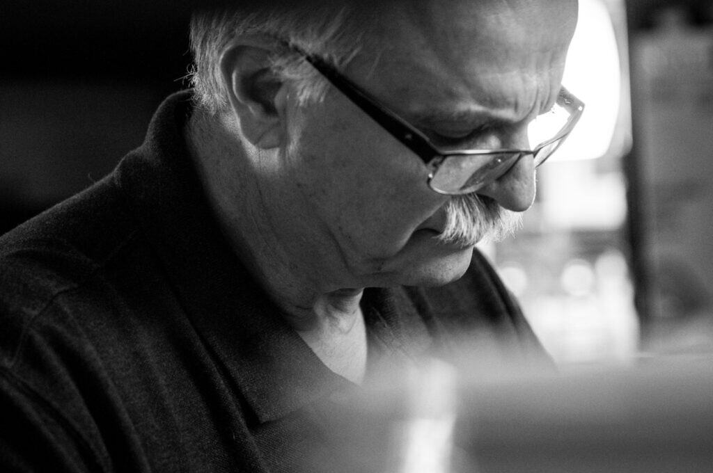 Delicious Supplì Inspired Kimchi Fried Rice Balls. 14 Black and white close-up of an older man with glasses and a mustache, looking down with a focused expression, wearing a dark collared shirt. The background is blurred.