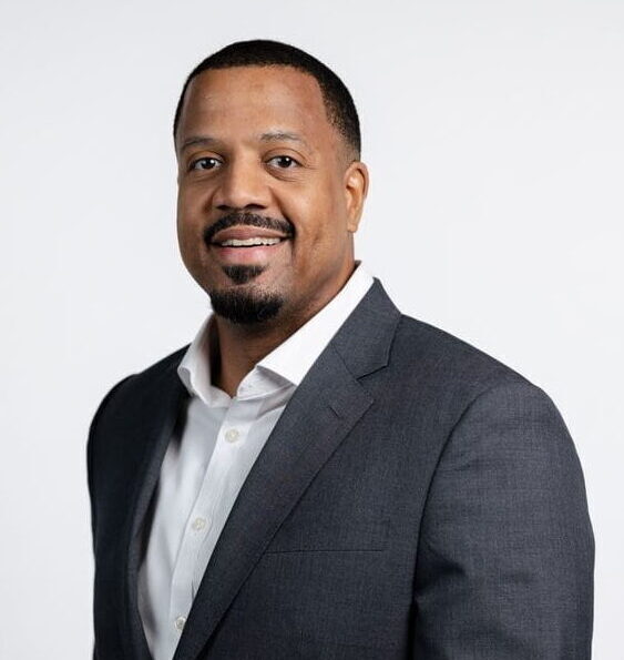 Headshot of a smiling Black man in a dark gray suit jacket and white shirt against a white background.