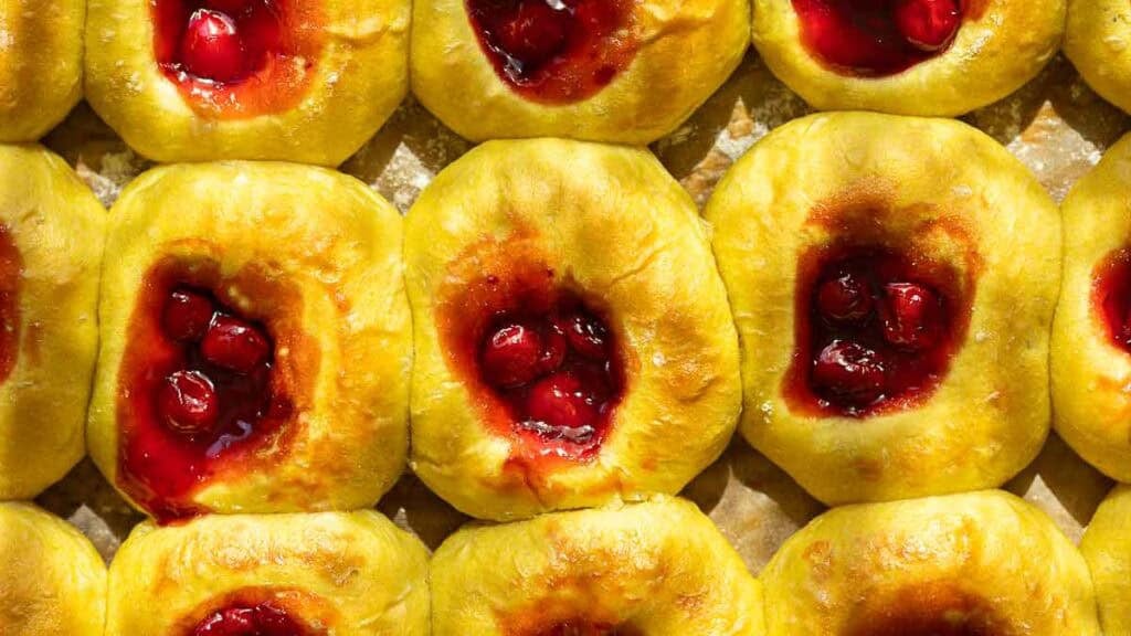 Easy Cherry Brioche Sweet Roll - Vegan Pastry. 13 Rows of golden cherry brioche sweet roll with centers filled with glossy red cherry filling, displayed close together on a baking sheet.