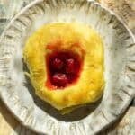 30+ AMAZING VEGAN Holiday Recipes Everyone's gonna Love. 27 A round cherry brioche sweet roll with a golden, fluffy crust and a center filled with red cherry filling sits on a textured ceramic plate.